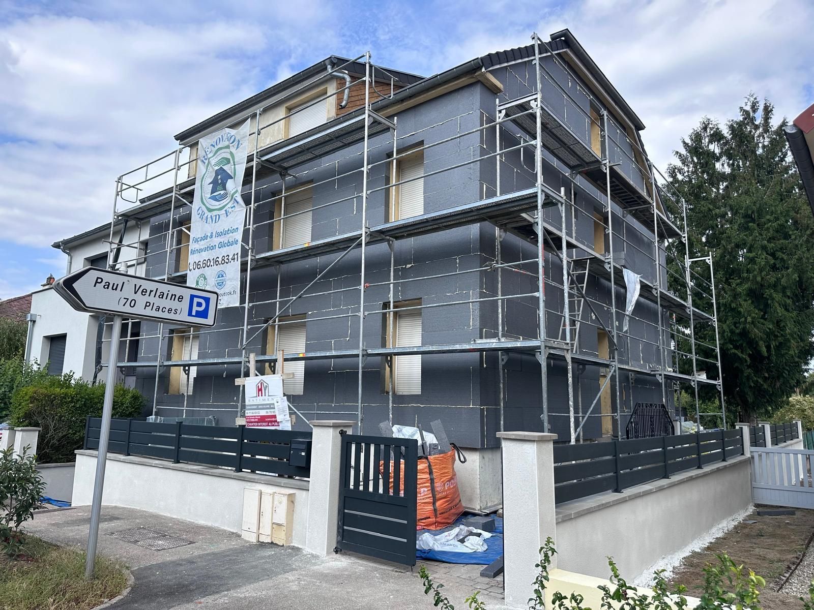 Maison en rénovation, recouverte d'isolant gris foncé, entourée d'échafaudages.