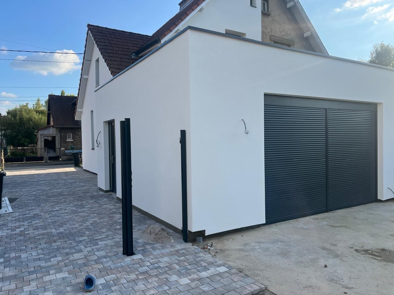 Maison en stuc blanc avec porte de garage noire et allée en briques.