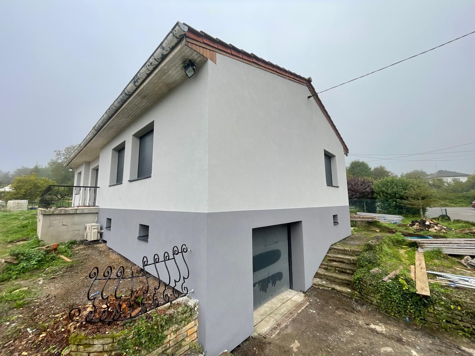 Maison à deux étages avec peinture extérieure grise et blanche, porte de garage et ciel couvert.