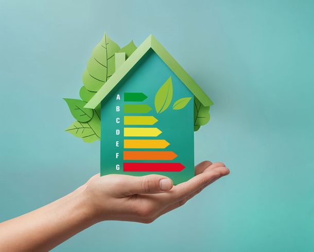 Main tenant une maison en papier avec une cote d'efficacité énergétique et des feuilles vertes.