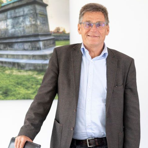 Ein Mann im Anzug und mit Brille lächelt in die Kamera.