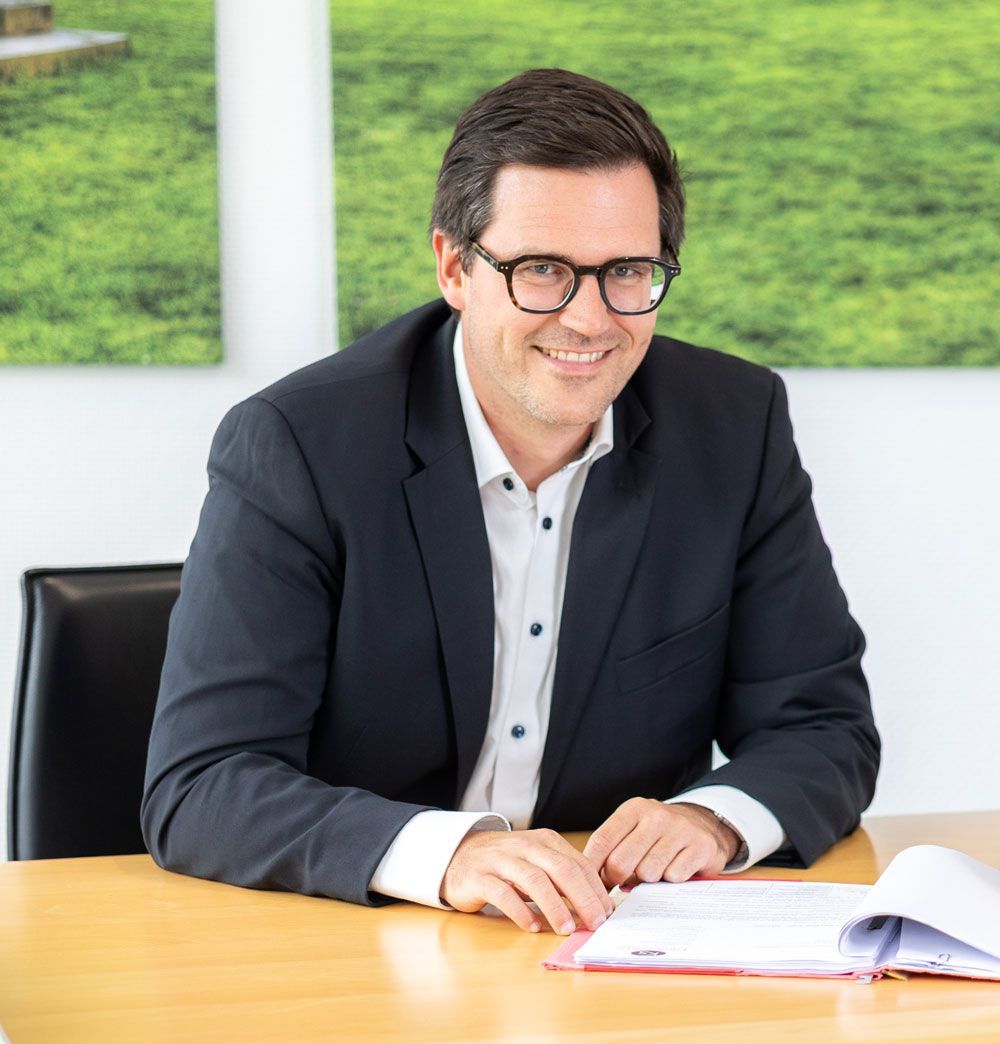 Ein Mann im Anzug und mit Brille lächelt in die Kamera.