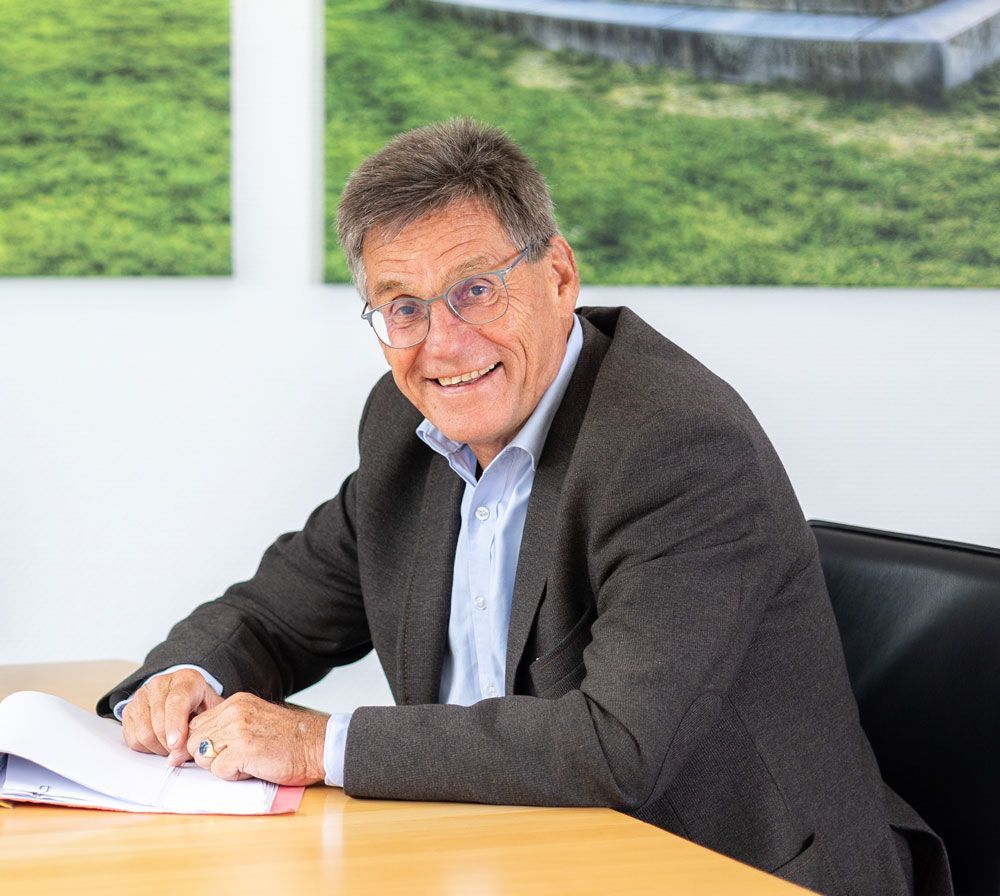 Ein Mann im Anzug und mit Brille lächelt in die Kamera.