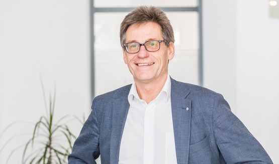 Ein Mann im Anzug und mit Brille lächelt in die Kamera.