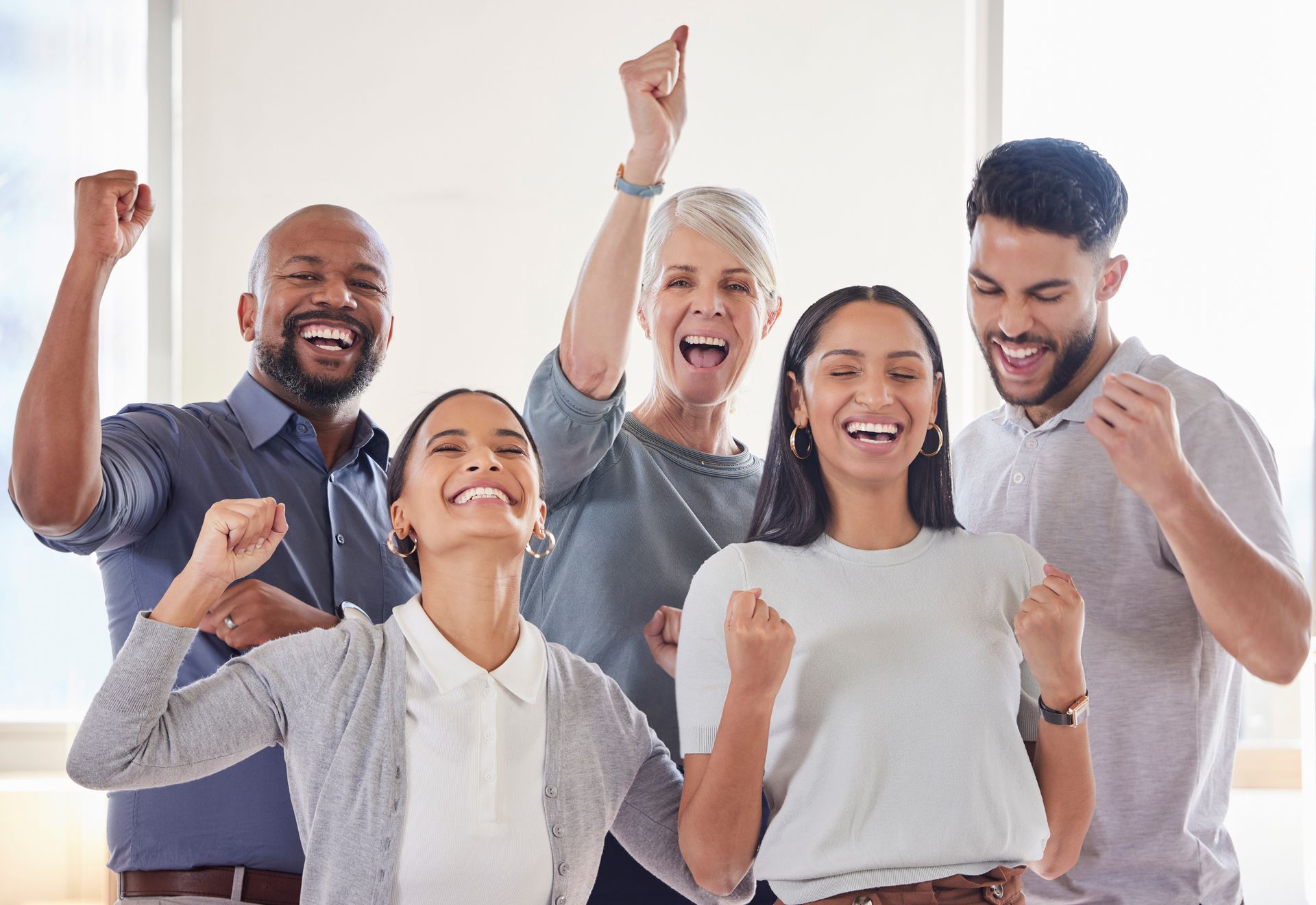 Cinq personnes d'une équipe en entreprise souriant et levant les bras au ciel