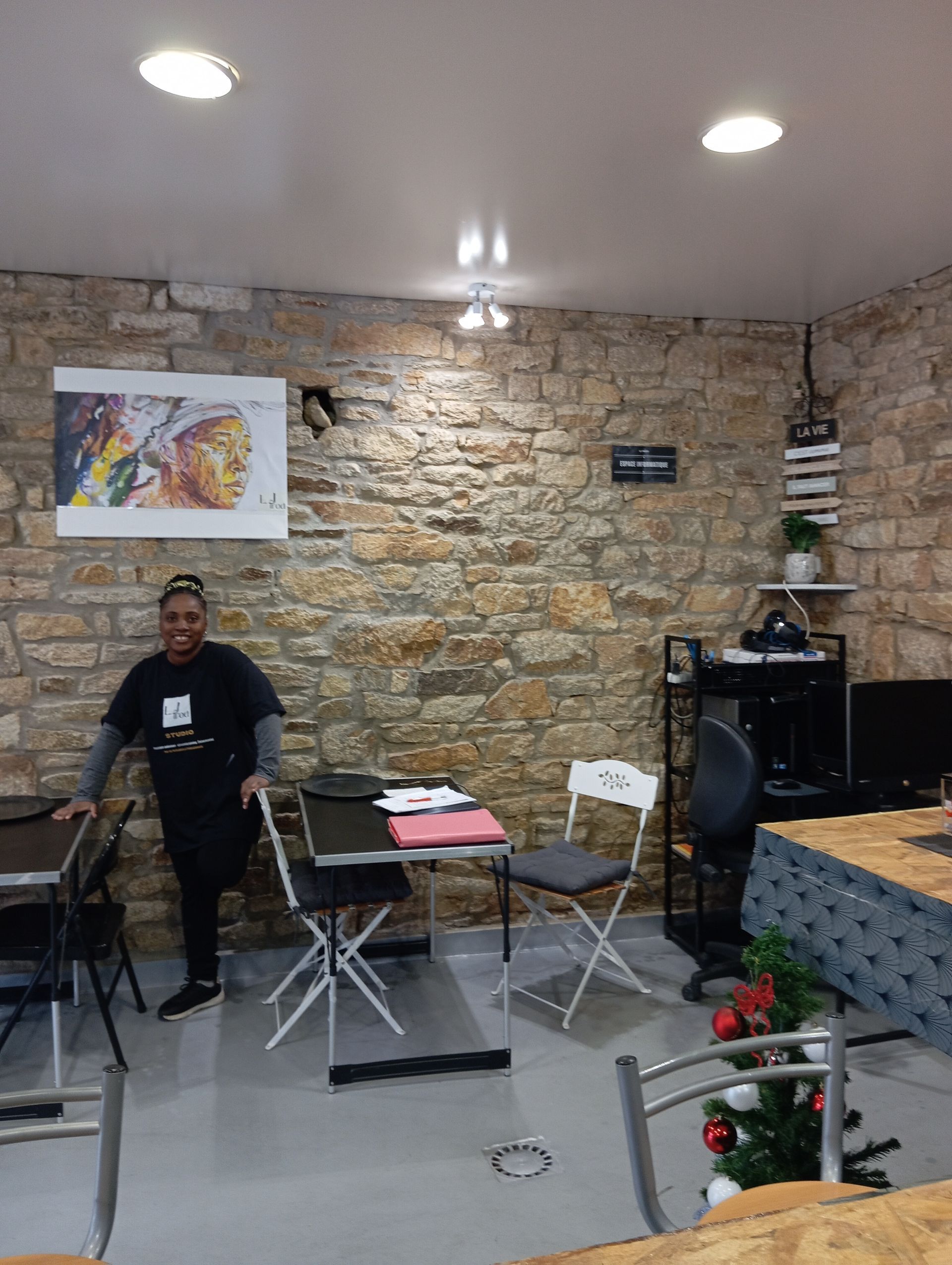 Partie Café avec mur en pierres, tables noires, chaises et fondatrice Lovely Jeune