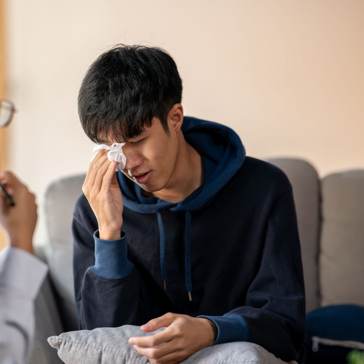 Une personne s'essuyant les larmes avec un mouchoir, assise sur un canapé pendant une séance de thérapie.