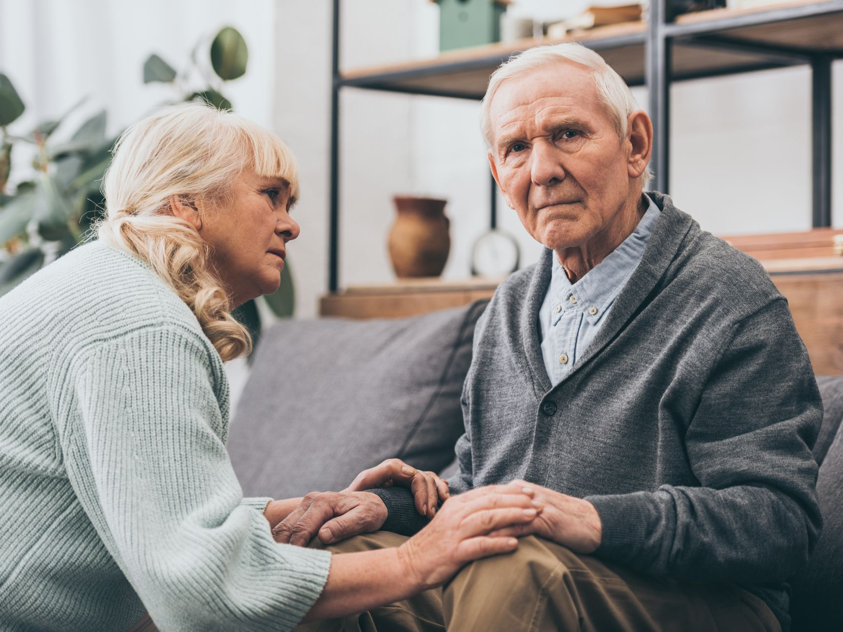 Une femme âgée tenant la main d'un homme agé sur un canapé. 
