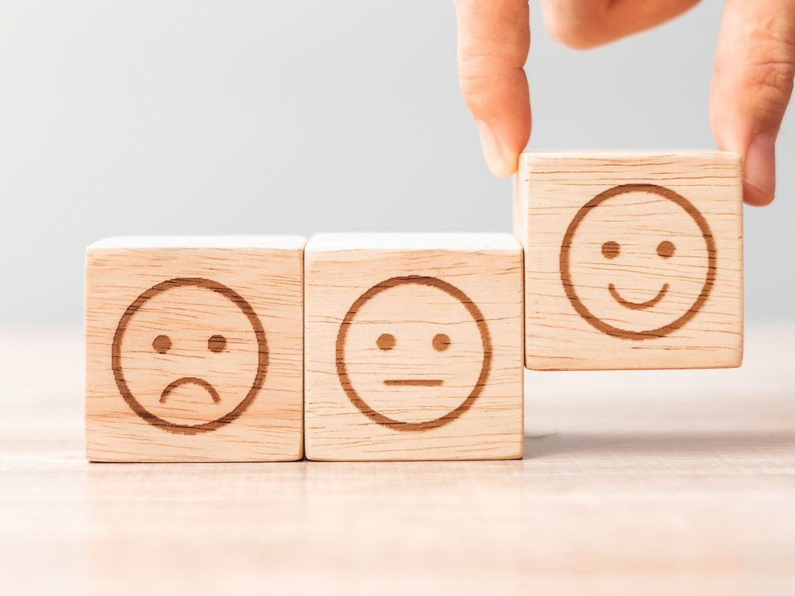 Agencement manuel de blocs de bois gravés de visages exprimant la tristesse, la neutralité et la joie.