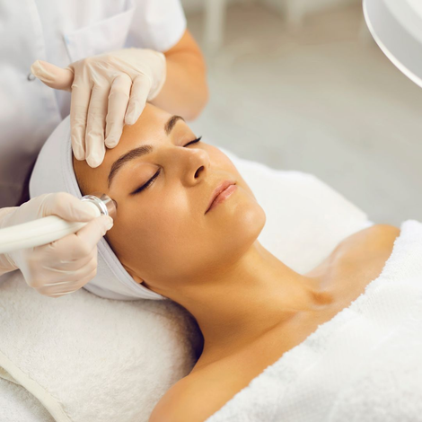 Mujer recibiendo tratamiento facial en un spa. El técnico le aplica un dispositivo en la frente, con ajuste blanco.