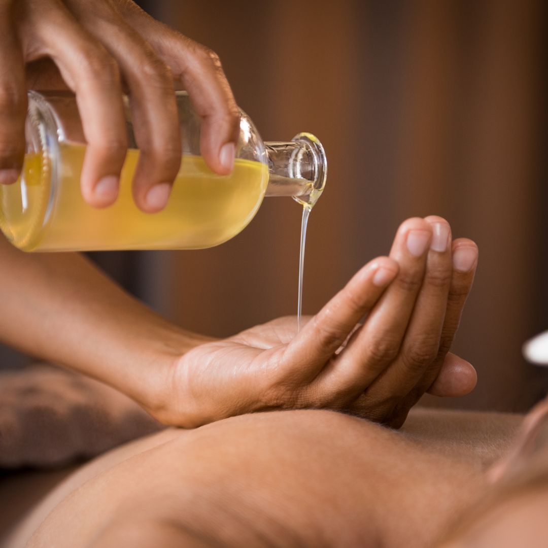 Persona vierte aceite en la mano de otra, preparándose para un masaje en un entorno tipo spa.