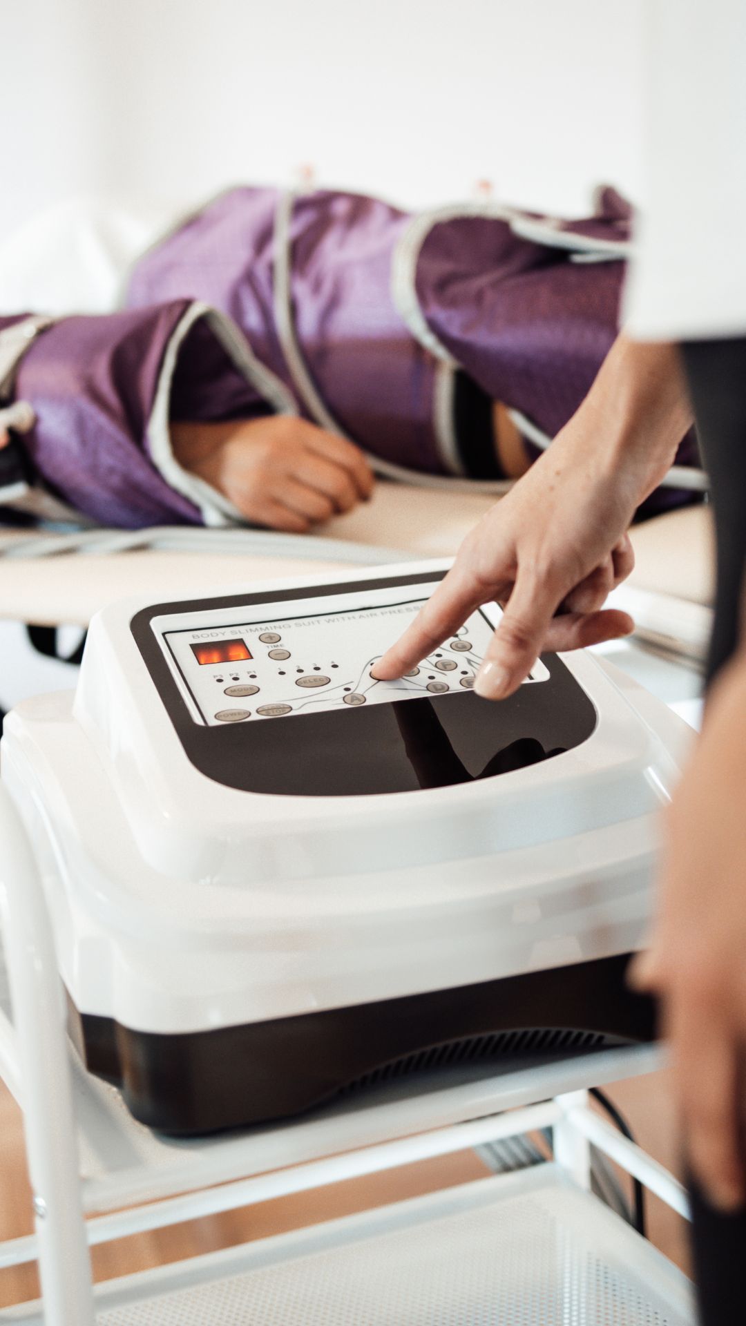 Persona con traje de compresión morado tumbada sobre una mesa, mientras una mano opera el panel de control de una máquina.