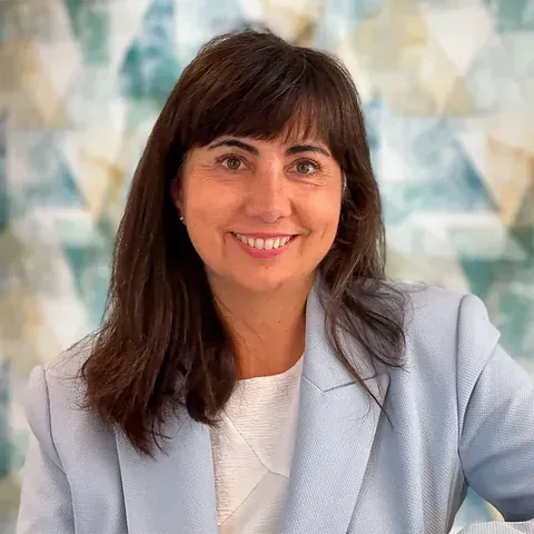 Una mujer con una chaqueta azul y una camisa blanca sonríe a la cámara.