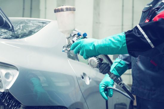 Un hombre que lleva guantes verdes está rociando pintura sobre un automóvil.