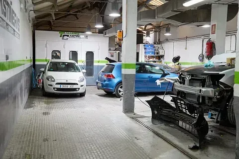 Un coche blanco está aparcado en un garaje al lado de un coche azul.