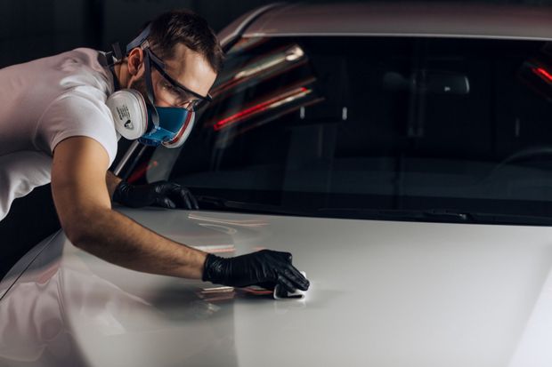 Un hombre que lleva una máscara y guantes está puliendo un coche.