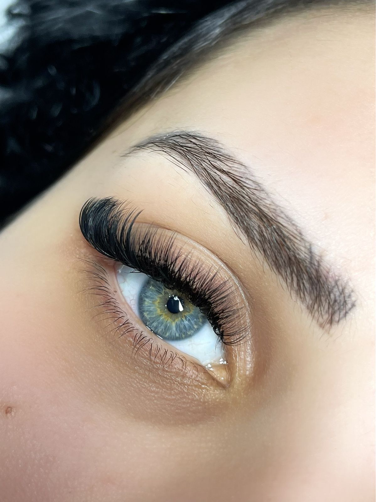 Nahaufnahme eines Auges mit dunklen, vollen Wimpernverlängerungen, heller Augenbraue und grüner Iris.