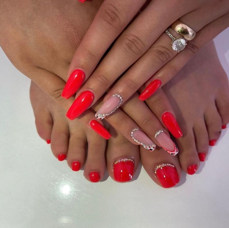 Hände und Füße mit leuchtend rotem Nagellack und Strasssteinen, Ringe an den Fingern.