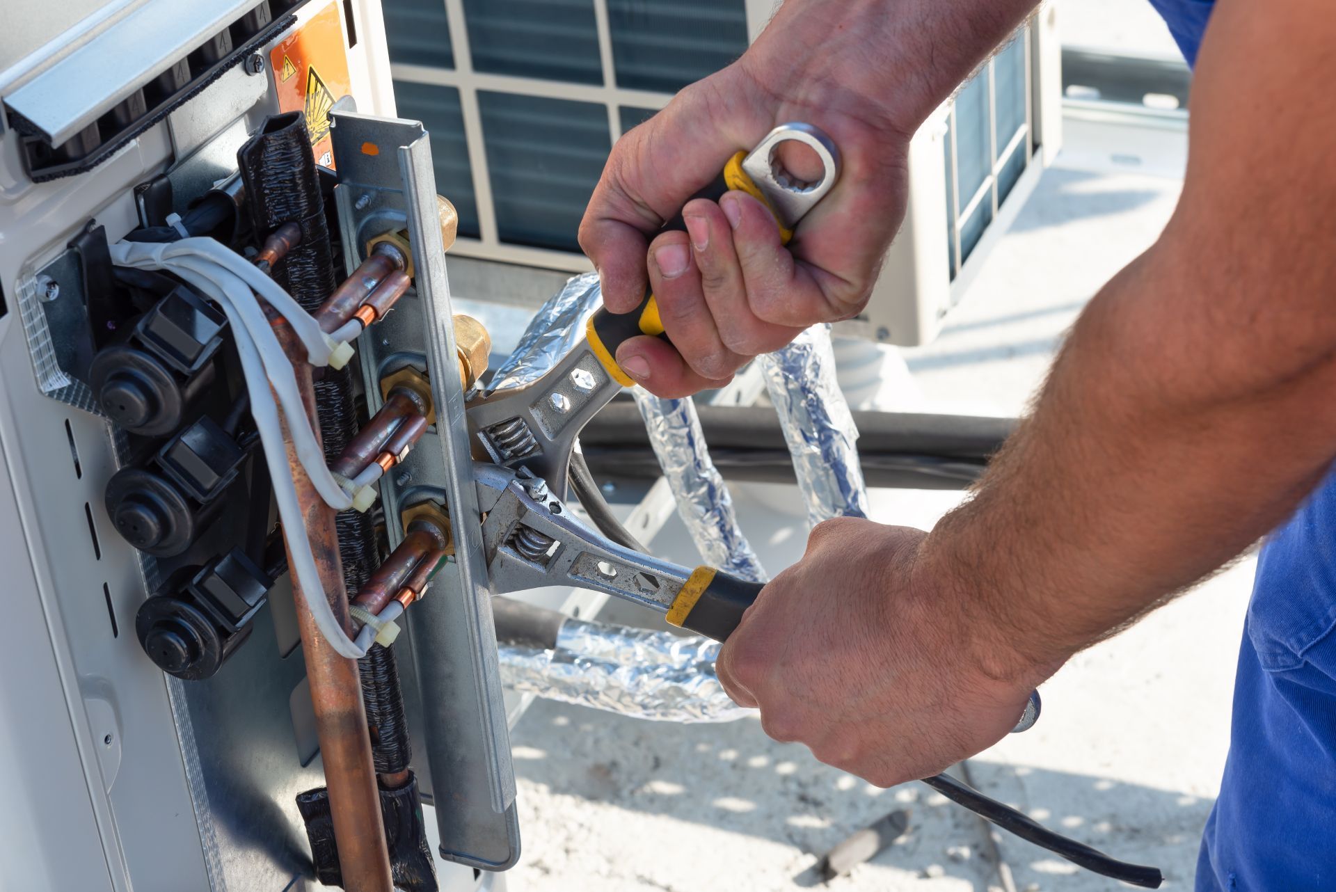 Ein Mann arbeitet mit einem Schraubenschlüssel an einer Klimaanlage.