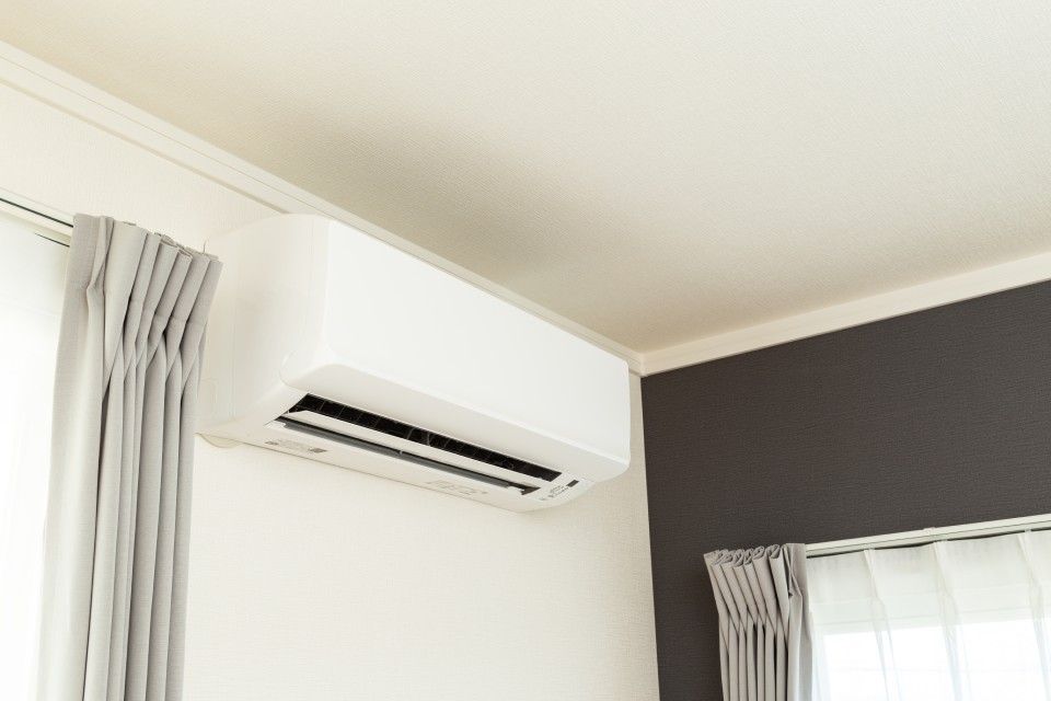In einem Raum neben einem Fenster hängt eine weiße Klimaanlage von der Decke.