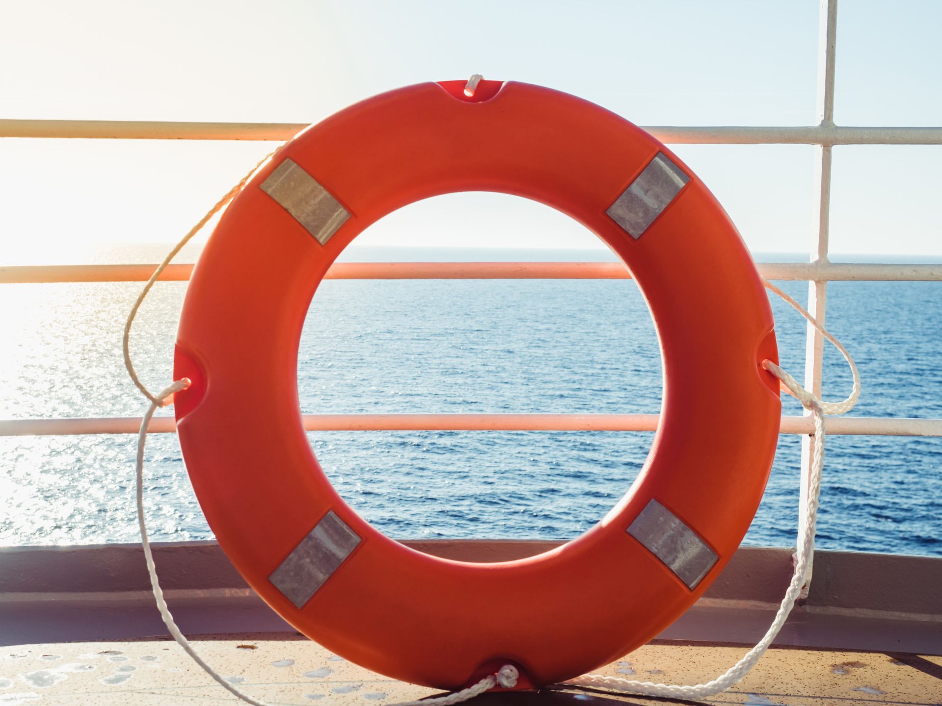 Un salvavidas naranja cuelga de una barandilla con vistas al océano.