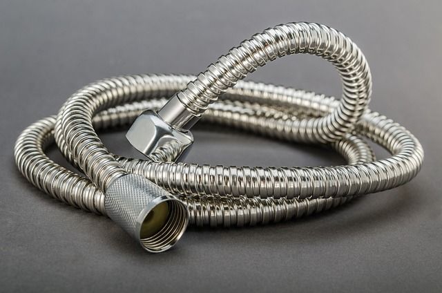 Un primer plano de una manguera de ducha de acero inoxidable sobre una superficie gris.