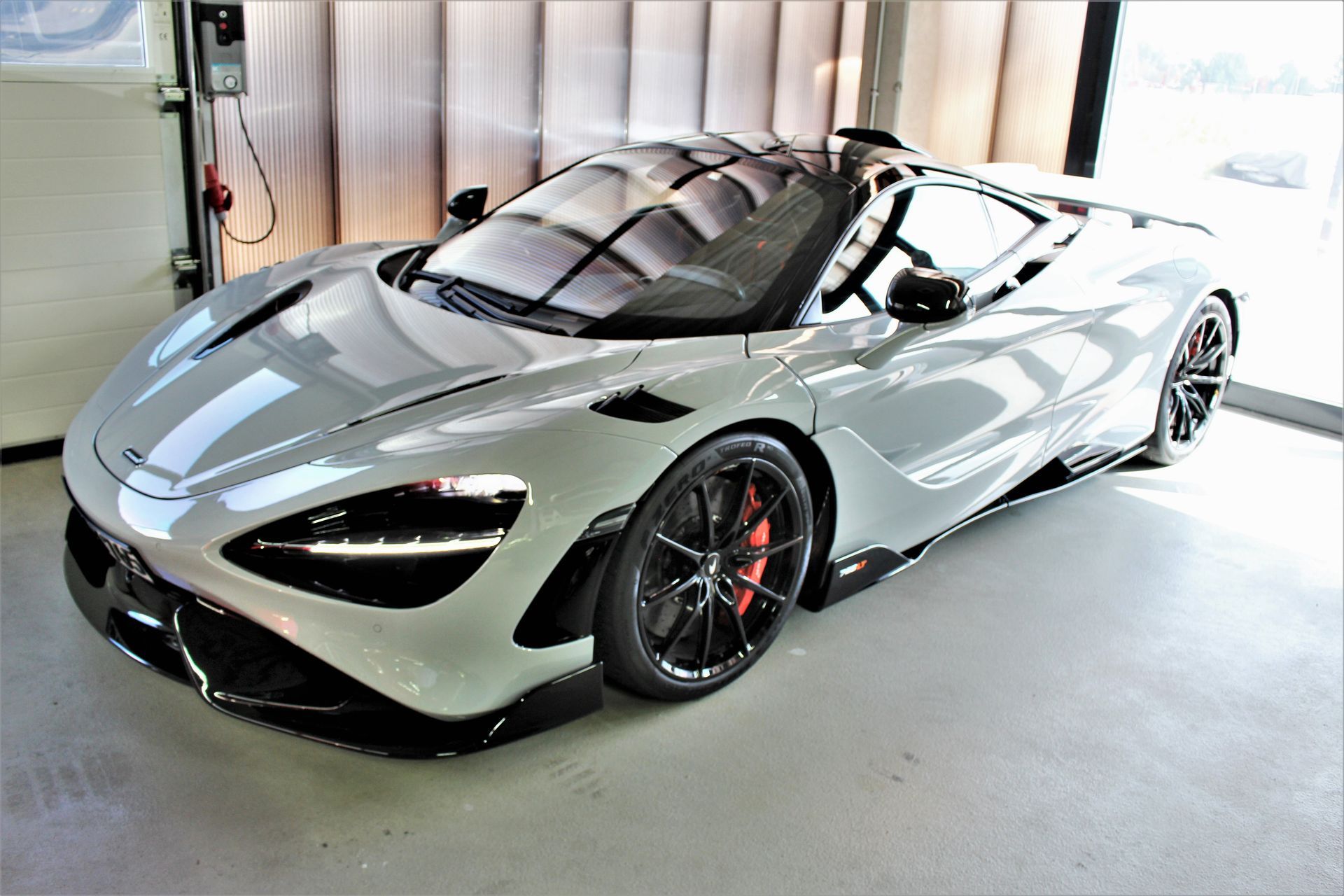 Silberner Sportwagen mit schwarzem Dach und roten Bremsen steht in einer Garage.