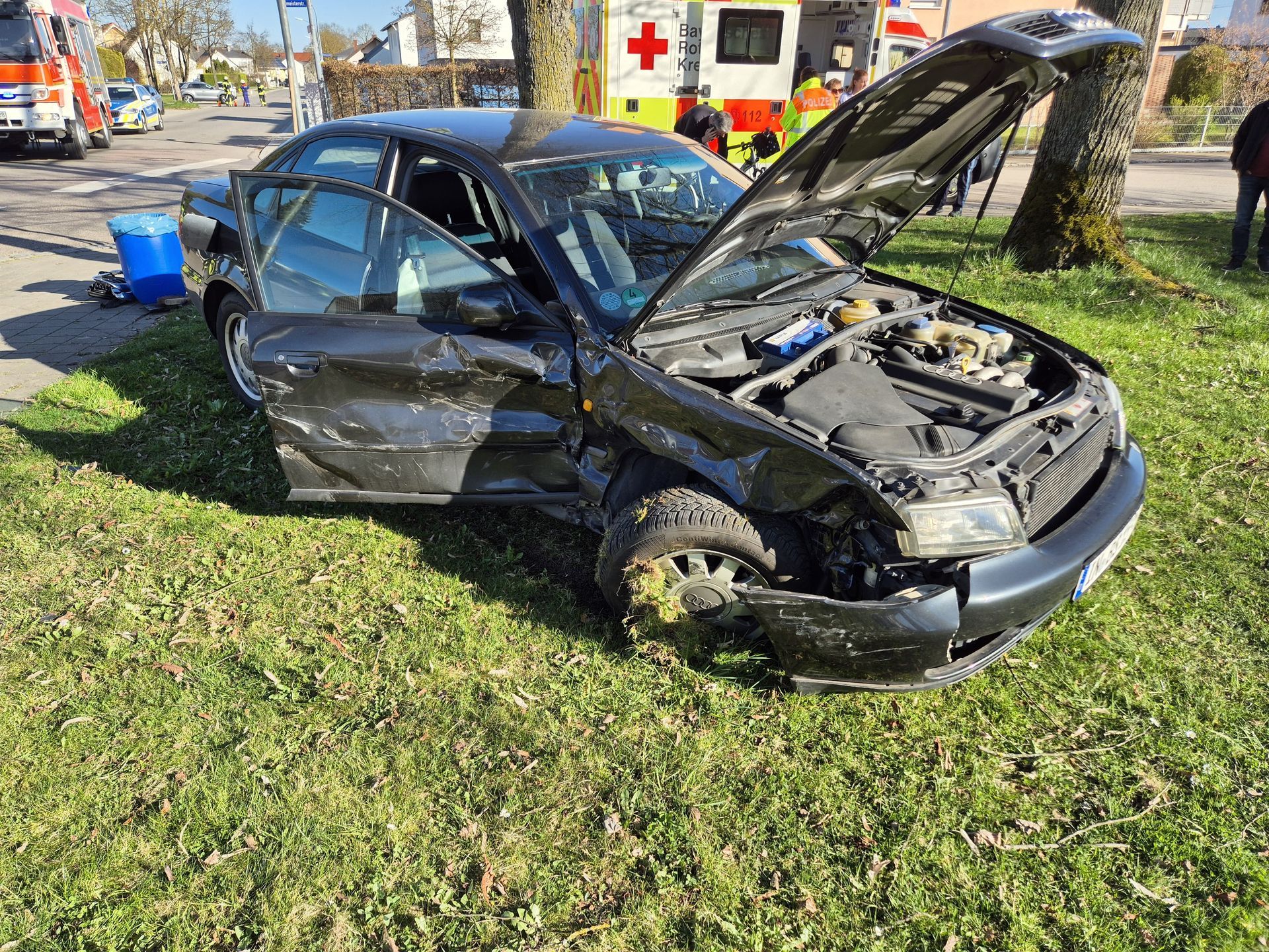 Schwarzes Auto mit geöffneter Motorhaube und stark beschädigter Fahrerseite.