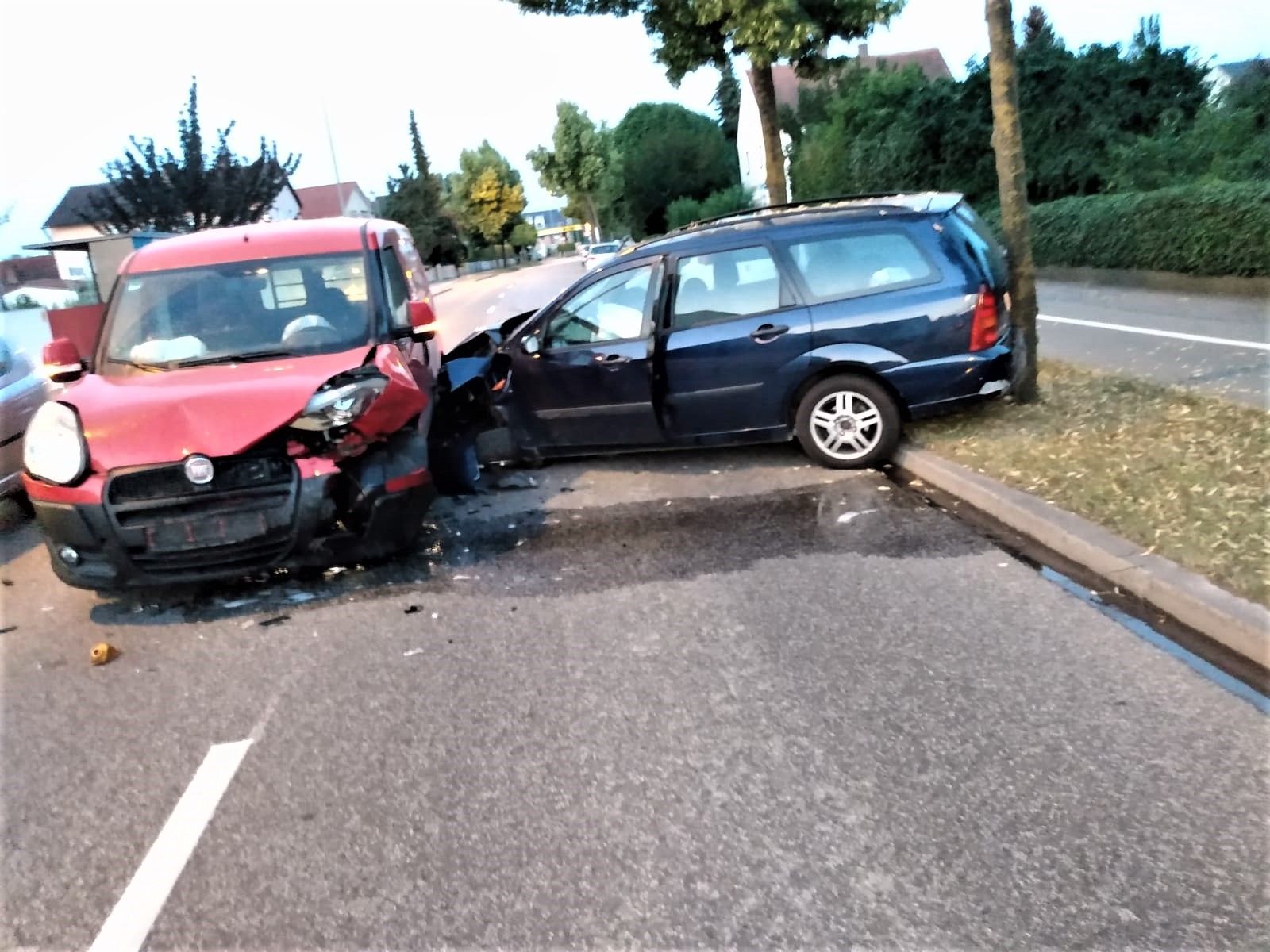 Roter Kleinwagen und blauer Kombi mit Frontschaden nach Zusammenstoß auf Straße, Kombi steht auf Gehweg.