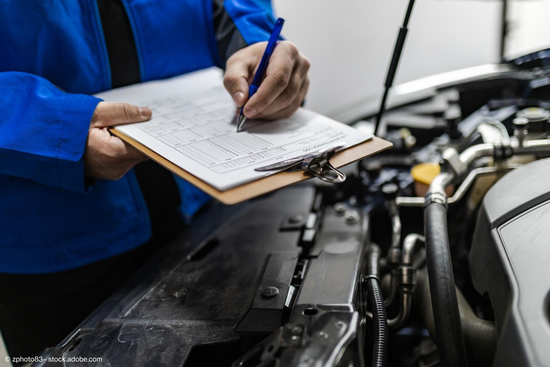 Ein Gutachter steht vor einer geöffneten Motorhaube und macht sich Notizen
