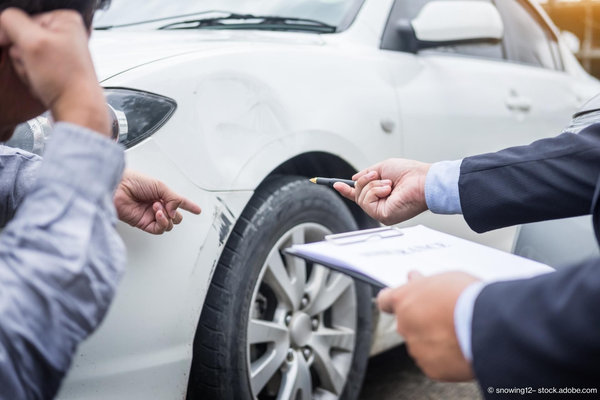 Ein Autofahrer zeigt auf einen Lackschaden, ein Gutachter steht mit einem Klemmbrett daneben