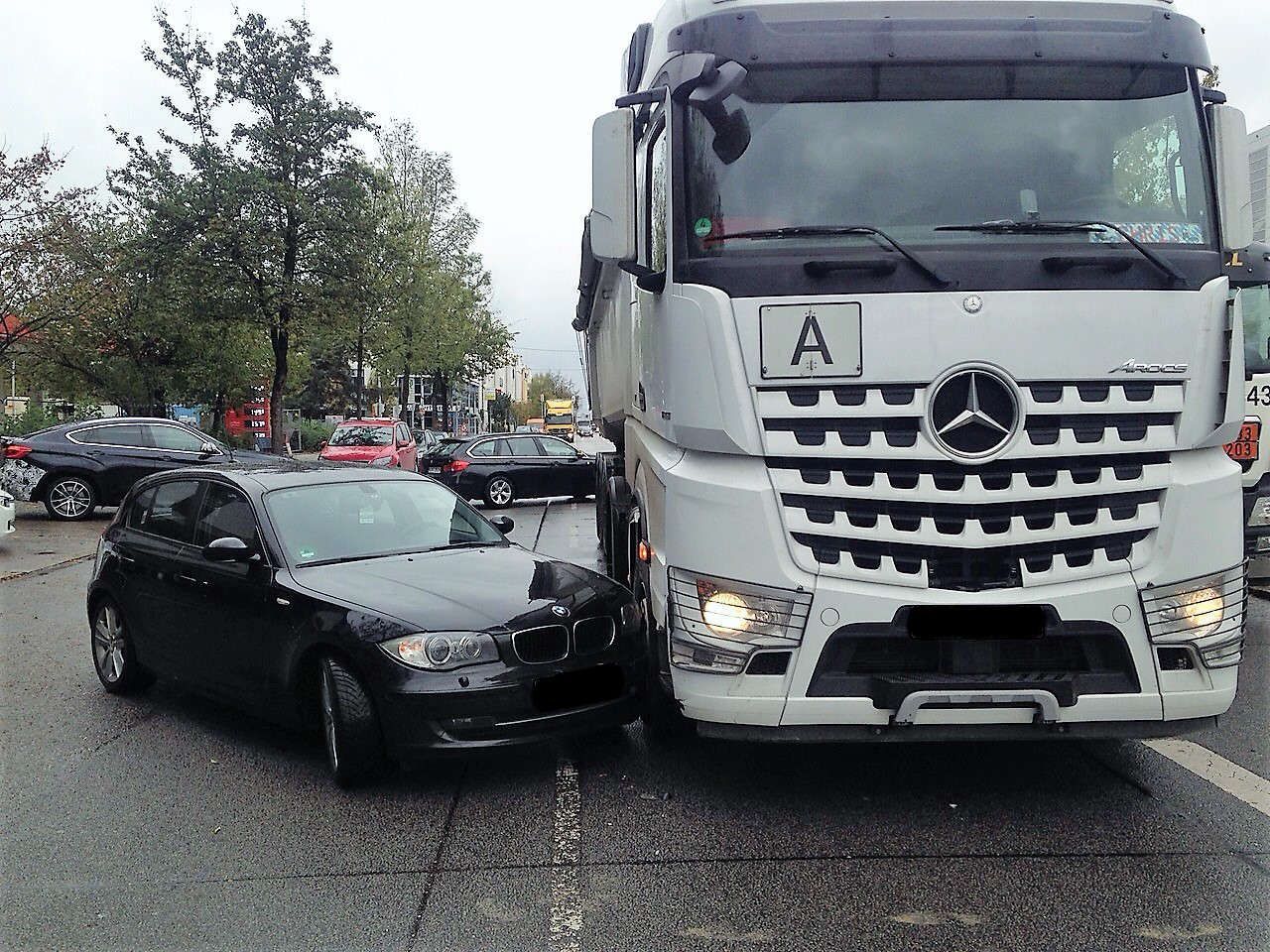 Schwarzes Auto steht sehr nah neben weißem Mercedes-Lkw mit deutschem Kennzeichen auf nasser Straße.