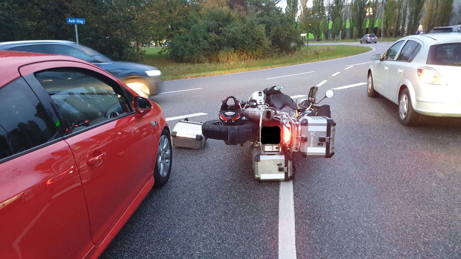 Motorrad liegt auf der Seite auf einer Straße, umgeben von mehreren Autos, eines davon rot, eines weiß.