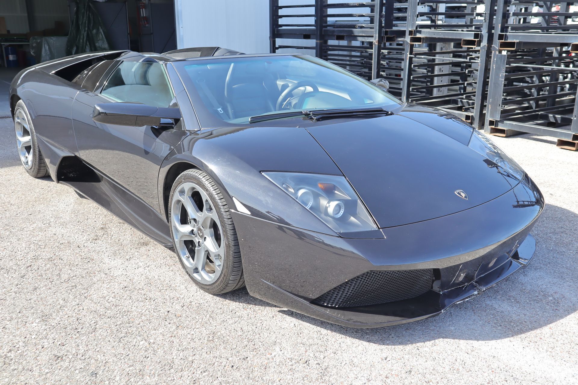 Schwarzer Lamborghini-Sportwagen mit scharfen Linien, zwei Scheinwerfern und glänzenden Felgen, geparkt auf Asphalt.