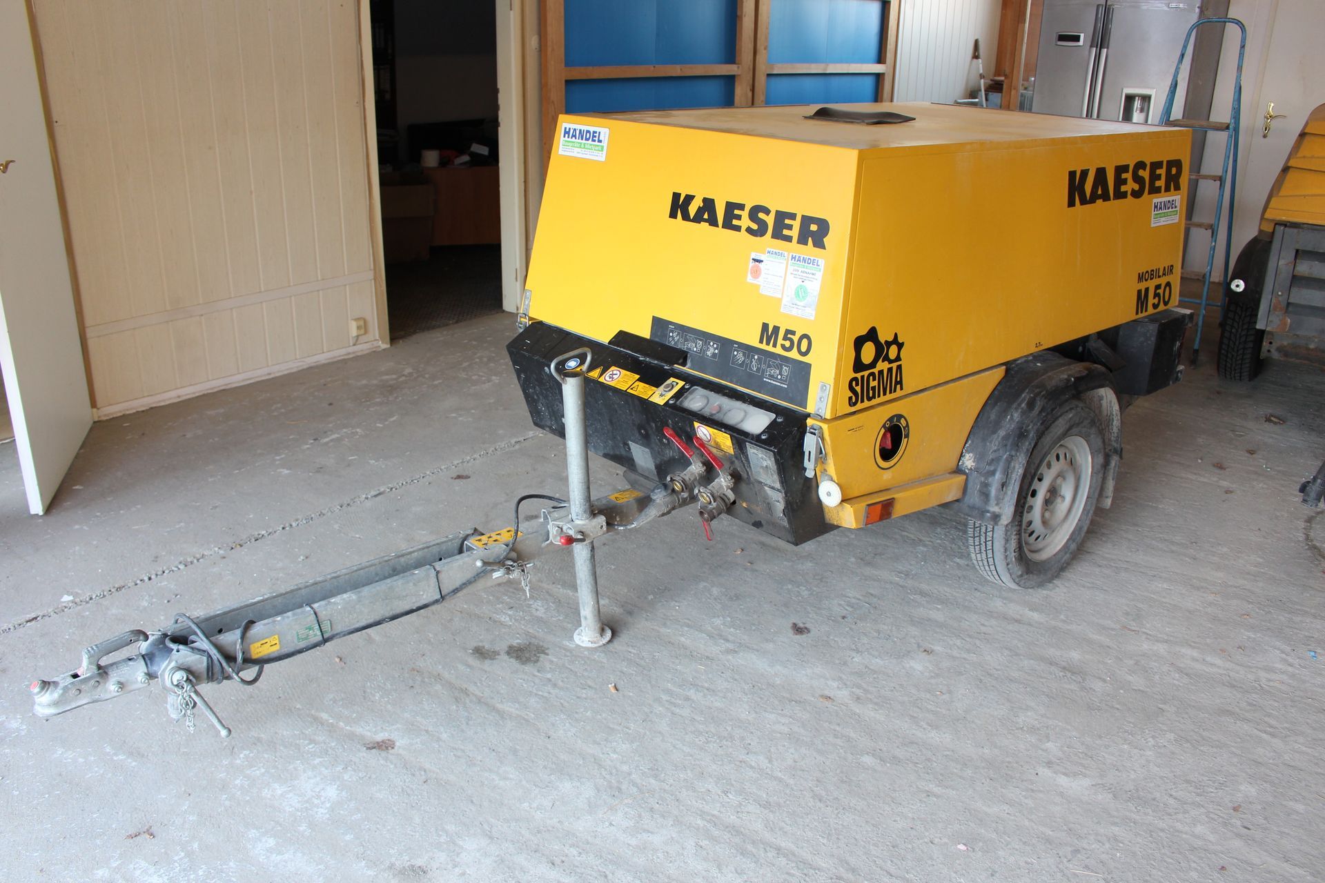 Gelb-schwarzer Kaeser M50 Kompressoranhänger mit Zugstange und Stützrad in einer Halle.