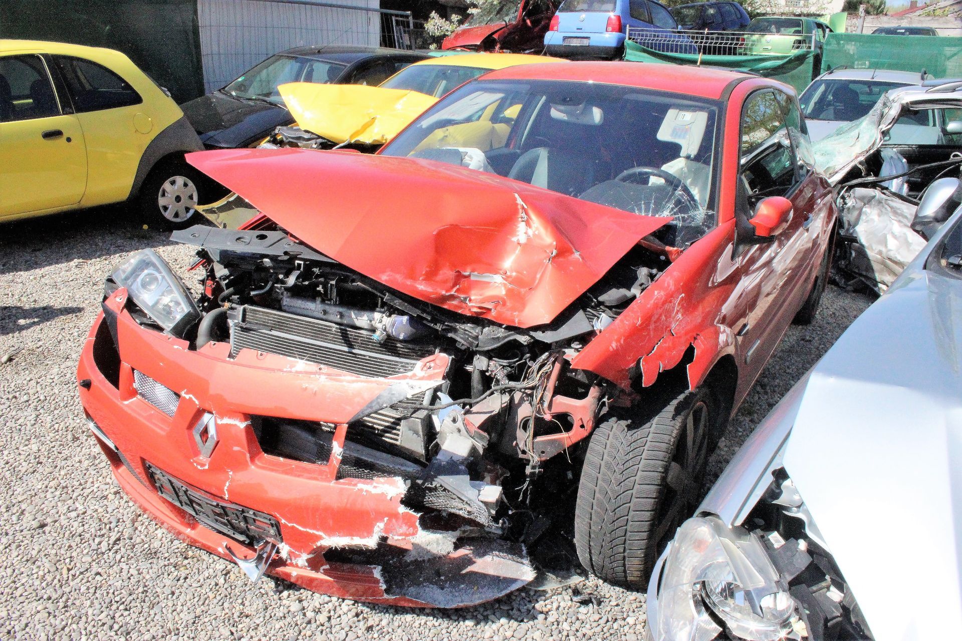 Roter Renault mit stark beschädigter Frontpartie, geöffneter Motorhaube und fehlendem rechten Kotflügel.