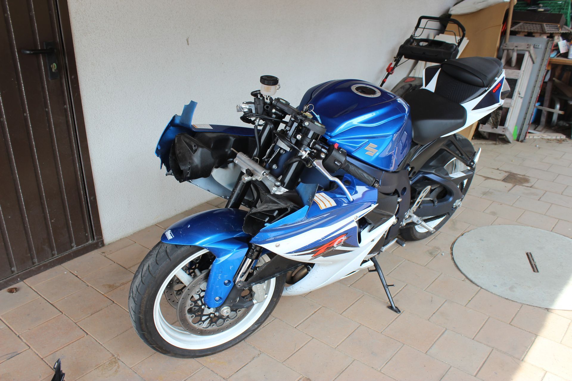 Blau-weiße Sportmotorrad mit fehlender Frontverkleidung steht in einer Garage auf Fliesenboden.