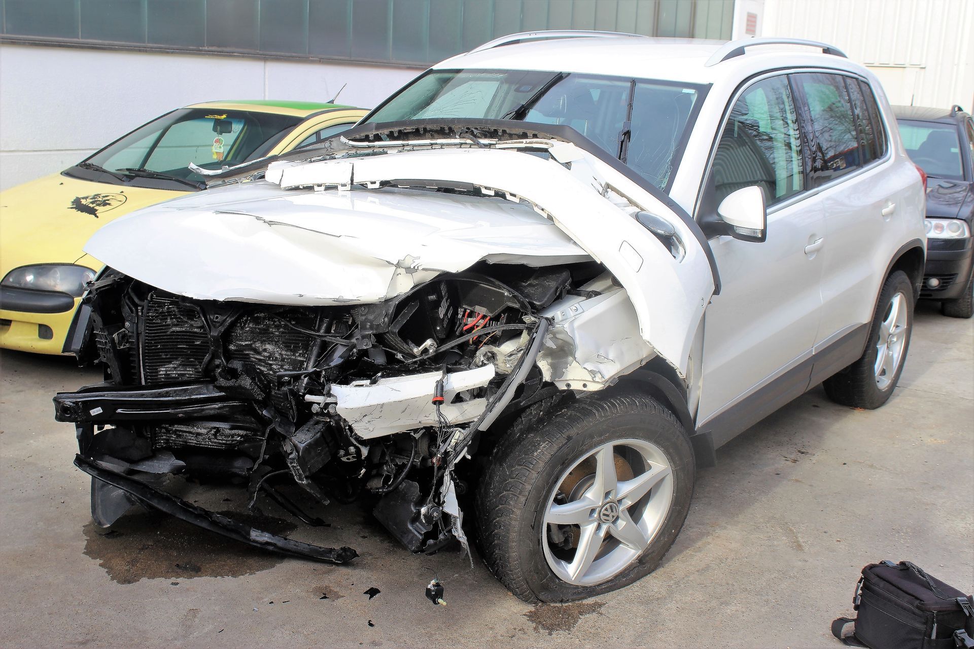 Weißer SUV mit stark beschädigter Frontpartie, Motorraum sichtbar, geparkte Autos im Hintergrund.