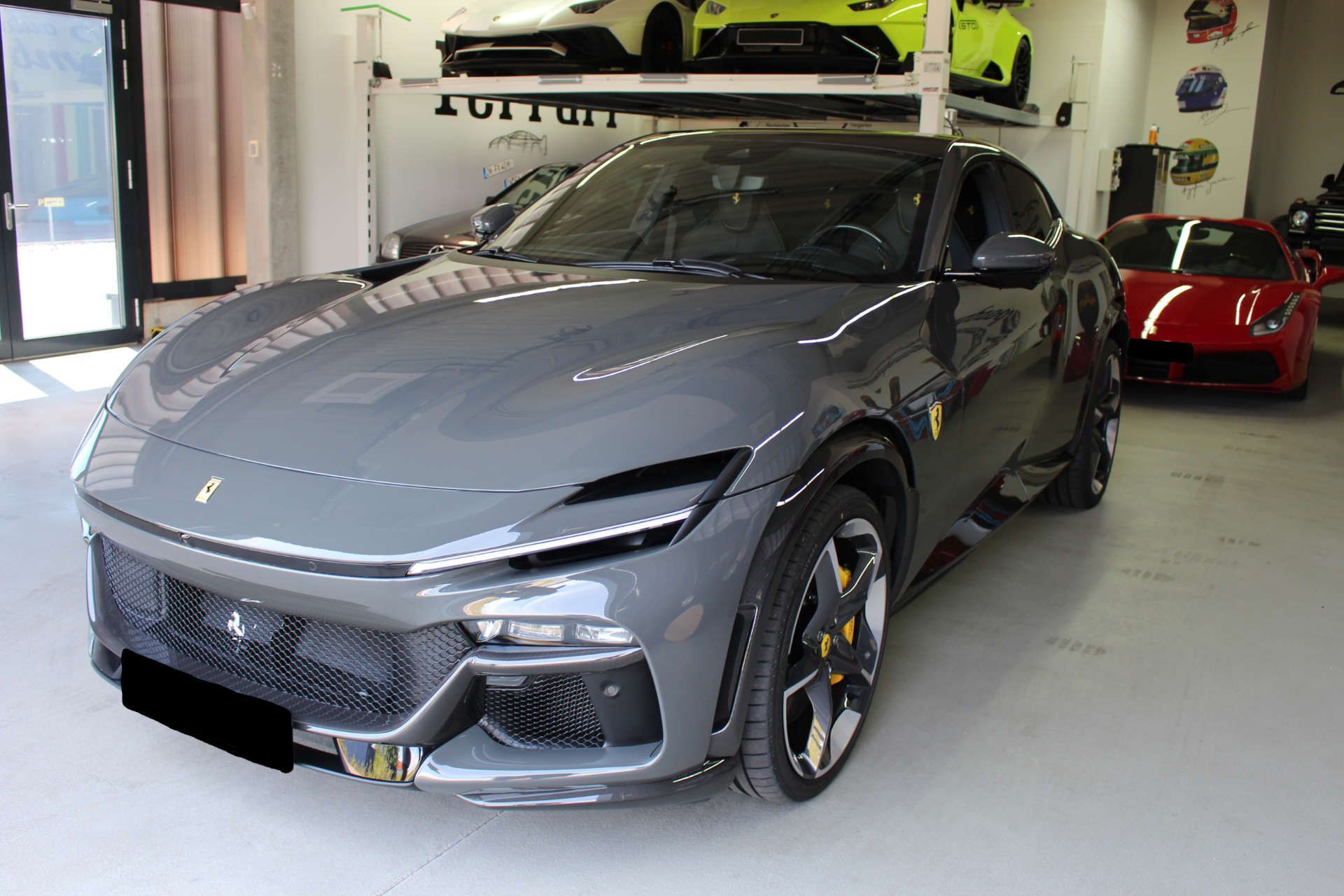 Grauer Ferrari-Sportwagen mit gelben Bremssätteln und deutschem Kennzeichen in einer Garage neben einem roten Ferrari.