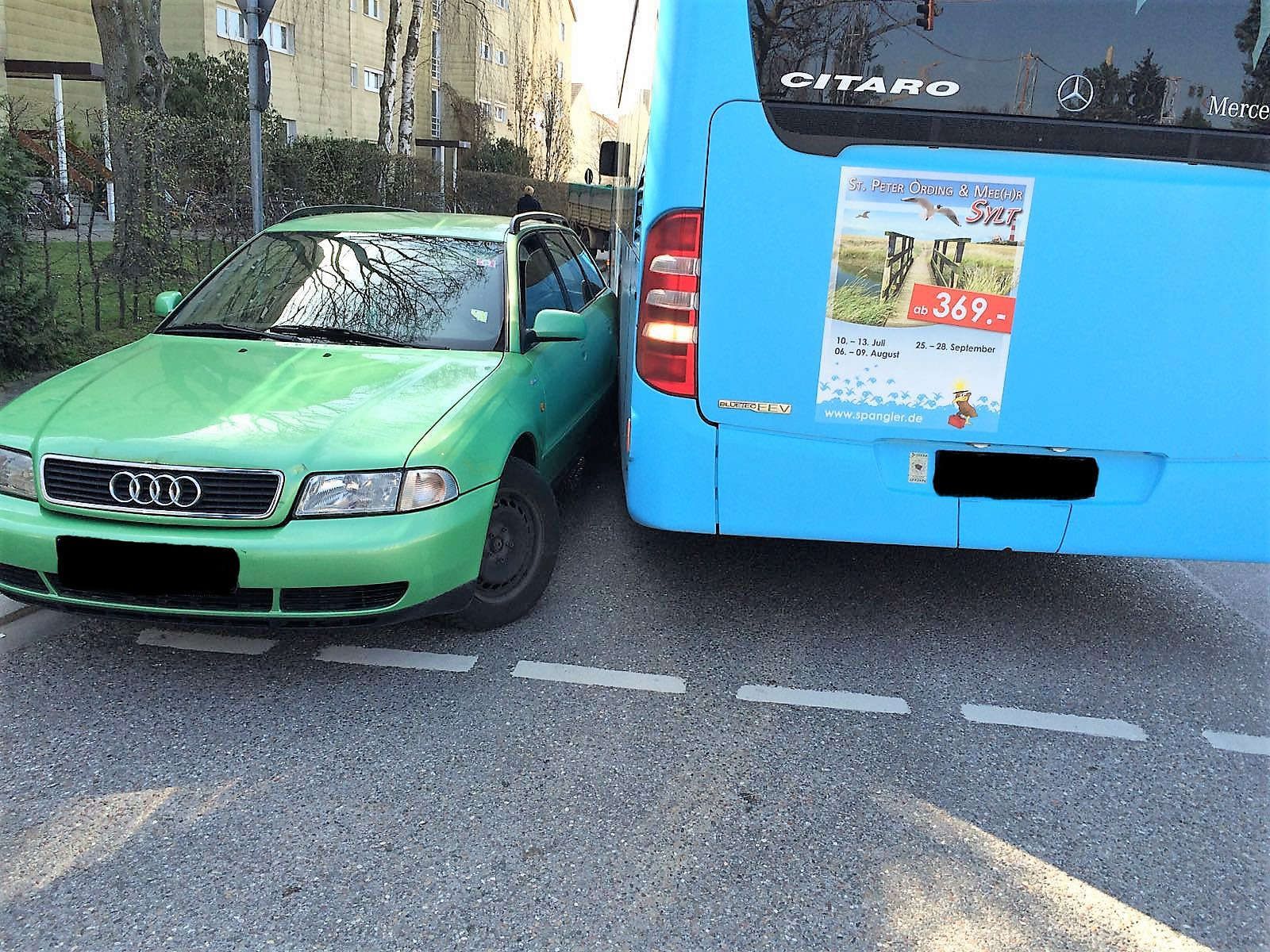 Grüner Audi-Pkw steht sehr nah neben einem blauen Mercedes Citaro Bus mit Werbeplakat.