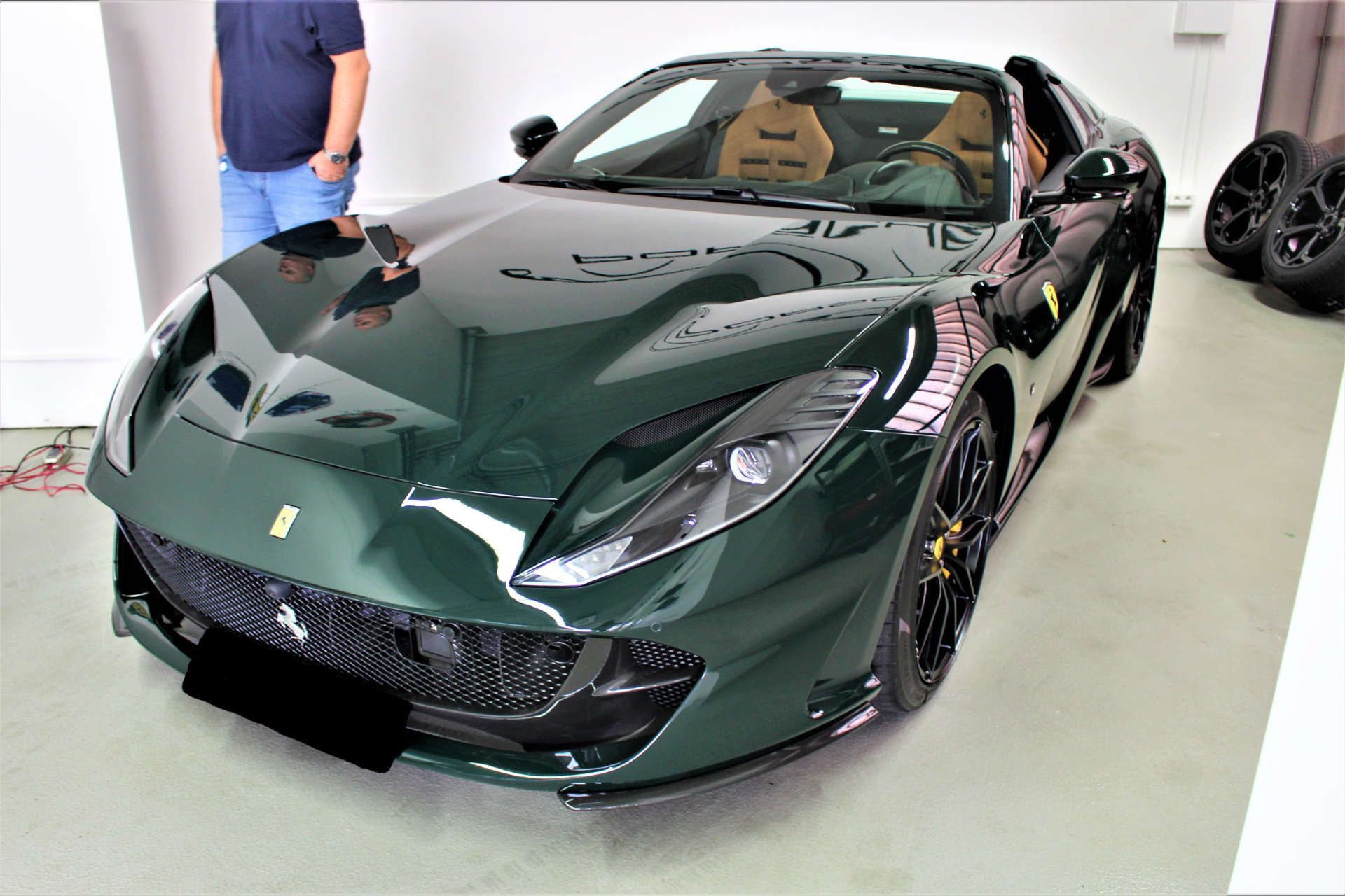 Dunkelgrüner Ferrari-Sportwagen mit beiger Innenausstattung, schwarzer Frontstoßstange und schwarzer Felge in einer Garage.