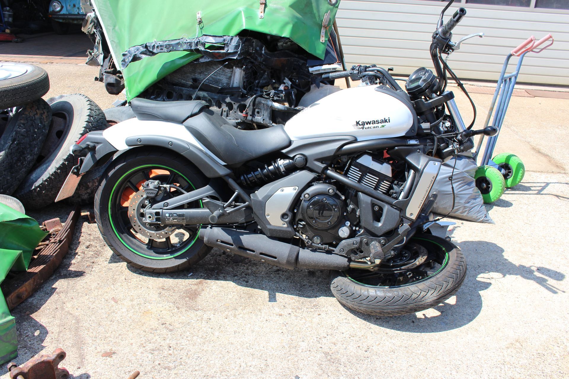 Weißes Kawasaki-Motorrad mit schwarzem Sitz und orangefarbenen Felgen, abgestützt auf einem umgefallenen Vorderrad.