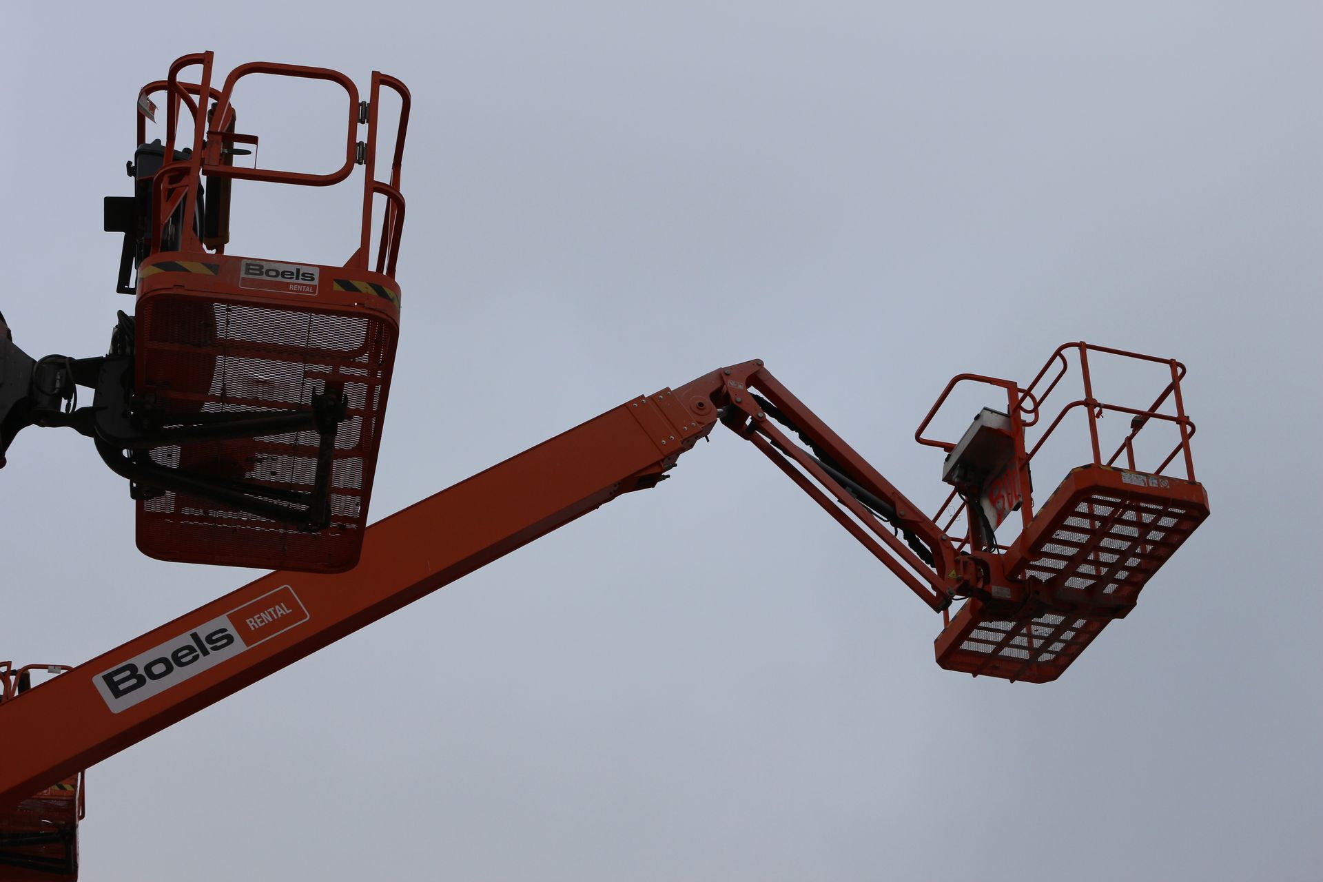 Zwei orangefarbene Arbeitsbühnen mit Gitterplattformen und dem Schriftzug 'Boels' vor grauem Himmel.
