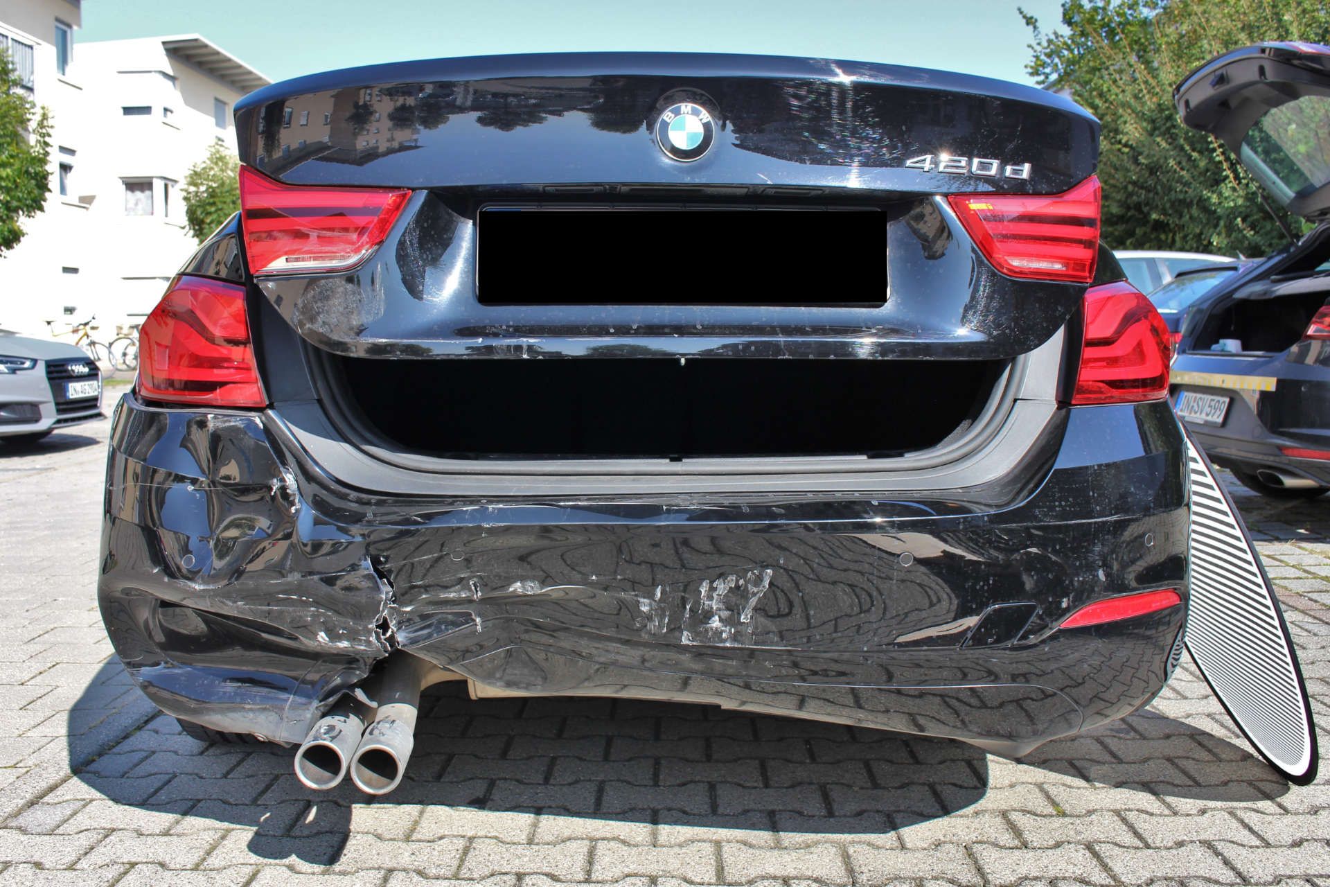 BMW 420d mit geöffneter Kofferraumklappe und deutlichen Dellen und Kratzern am linken hinteren Stoßfänger.