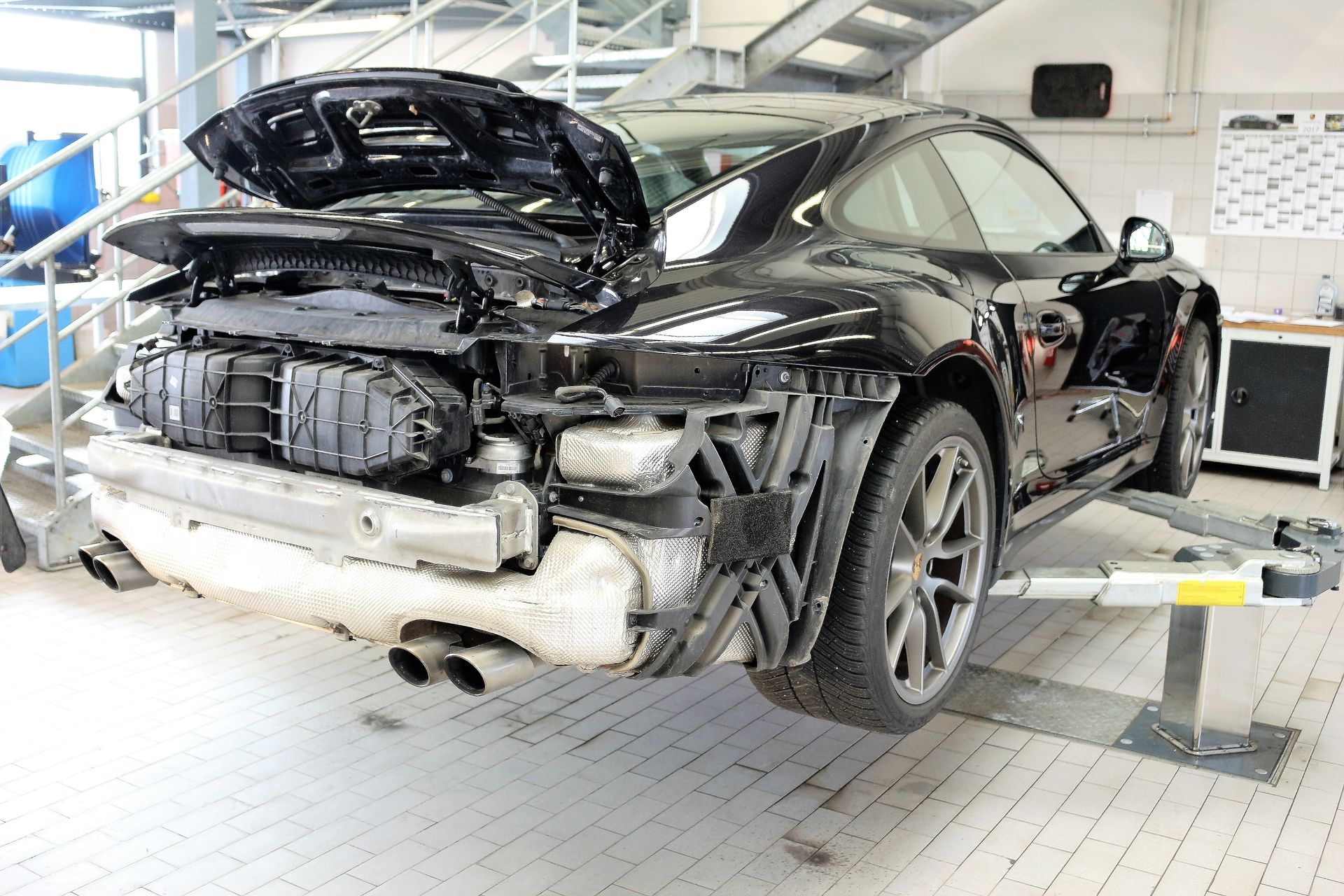 Schwarzer Sportwagen mit geöffneter Motorhaube und fehlender hinterer Stoßstange in einer Werkstatt.