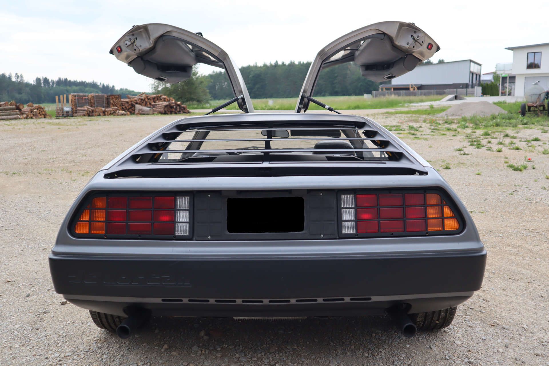 Heckansicht eines silbernen DeLorean-Sportwagens mit geöffneten Flügeltüren und kalifornischem Kennzeichen 'OUTATIME'.