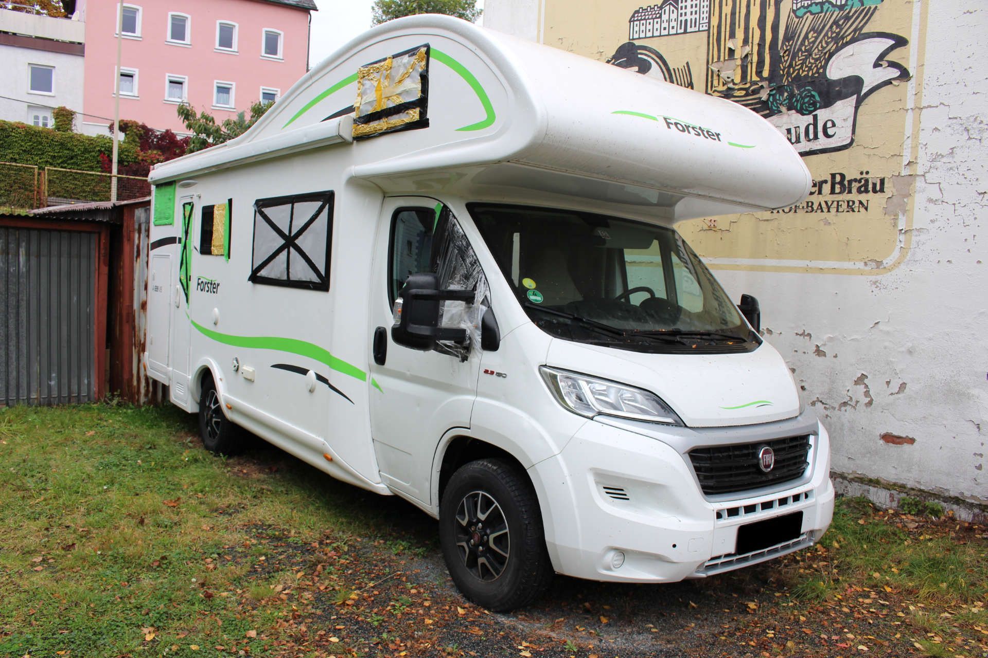 Weißes Wohnmobil der Marke Forster mit grünen Zierlinien, schwarzem Außenspiegel und deutschem Kennzeichen.