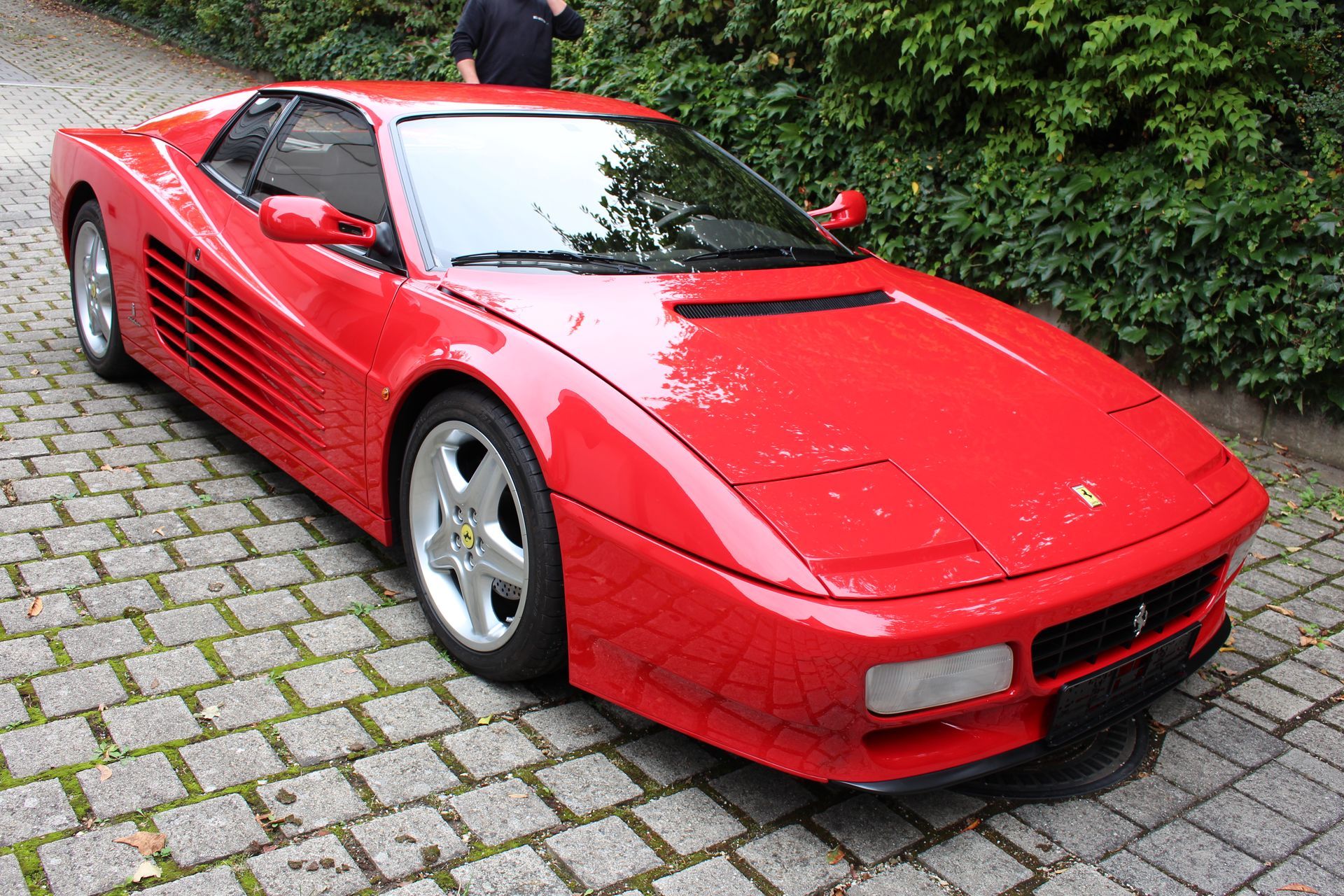 Roter Ferrari-Sportwagen mit geschlossener Motorhaube auf gepflastertem Weg.