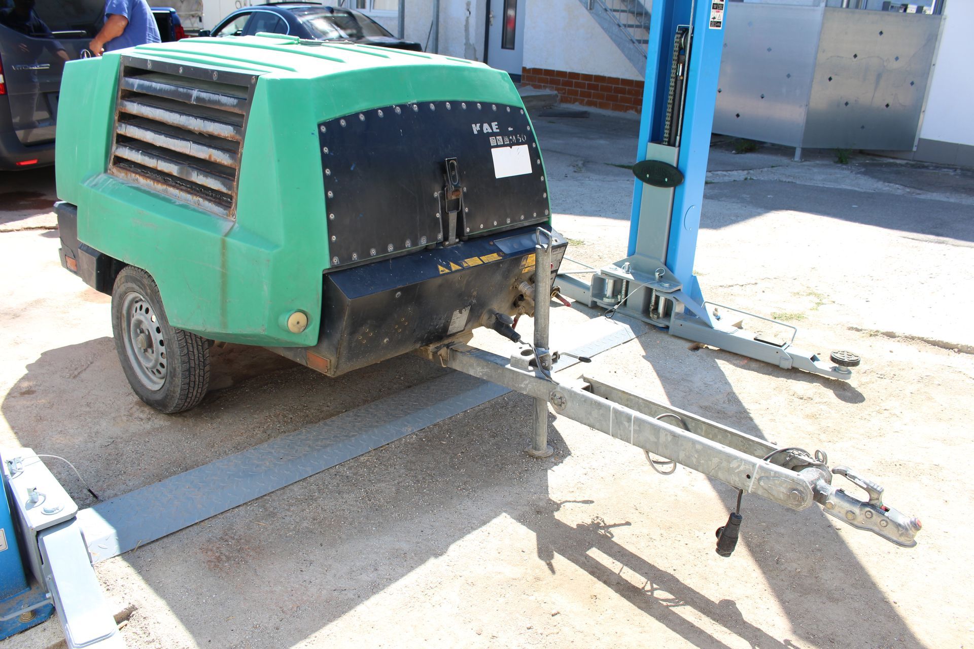 Grüner, mobiler Kompressor mit schwarzer Frontplatte, montiert auf einem Anhänger mit zwei Reifen und Zugstange.