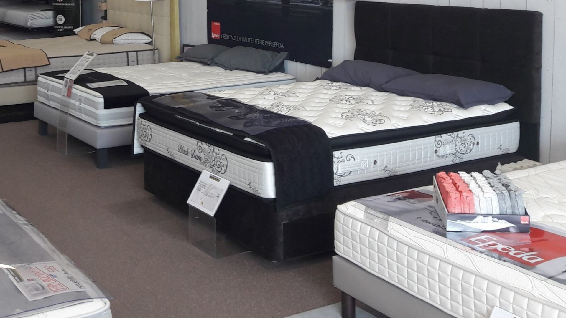 Des matelas exposés en magasin, de différentes tailles et styles, certains avec têtes de lit et literie
